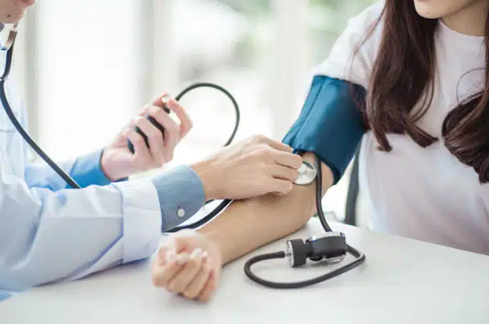 Clinician measuring a patient’s blood pressure with a cuff and stethoscope.