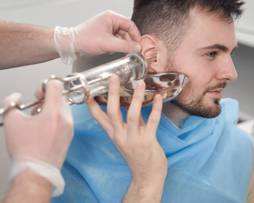 Close-up of a clinician performing ear irrigation on a man with a metal ear cleaning device.